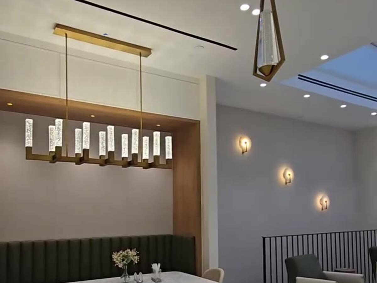Breakfast nook with green banquette, linear chandelier and marble tables under a skylight